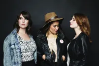 Three women pose in front of a black wall.