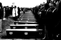 People stand in front of a row of coffins.