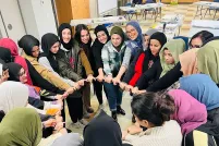 A group of smiling Muslim women in a circle with linked hands.