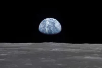 View of earth rising above the lunar horizon, showing the blue and white planet against the dark backdrop of space as seen from the moon’s surface.