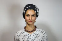 A Pakistani woman, Anam Abbas, in a black and white headwrap, red lipstick, chunky brown collar necklace and black-and-white blouse looks forward with a bemused expression.