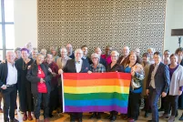 Twenty-eight members of the LGBT Purge Fund Board and LGBTQ2+ National Monument Advisory Committee standing together and holding a rainbow flag, at the first Monument visioning session in 2019.
