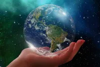 A stylized image shows a human hand gently holding a glass orb of the earth. The background is a night sky with stars and bright green northern lights.