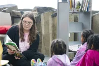 An adult sitting on the floor reading a book to three children sitting in front of them.