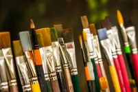Various sizes of paint brushes standing in a paint-brush holder against a blurred green backdrop.
