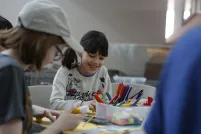 Children of different ages are sitting around a table doing crafts.