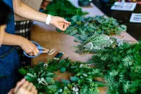 A close-up of two people making a wreath. One person is holding clippers and is about to cut some wire.