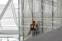 Male worker wearing safety vest suspended from ropes cleaning windows from a high height.