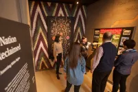 A guide speaks to a small group of people in a museum exhibit space. The space includes a wall featuring a Métis artwork and a text panel that reads “A Nation Reclaimed”.