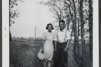 A young Japanese Canadian couple pose in a field with trees in the background.
