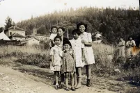 Black-and-white image of women and children standing on a gravel road in front of a field.