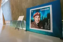 An enlarged Canadian stamp showcases a man with a red military beret with an aurora borealis and darkened forest in the background.