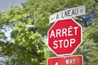 A stop sign and street sign in both English and French are seen in front of trees.
