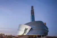 The exterior of the Canadian Museum for Human Rights, seen in the sunset against the city skyline.