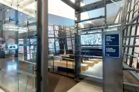 Uneven glass walls surround a theatre with a screen and 4 benches facing it. Outside the theatre entrance is a sign indicating the film selected to play.