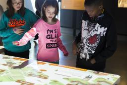 A group of three children stand in front of an interactive table.