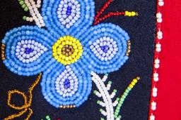 A blue beaded flower on a black and red background.