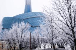 An unusual building surrounded by a glass "cloud" and topped by a tower. It is surrounded by snow and bare trees.