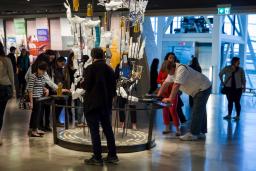 A large number of people in a gallery examining a display comprised of several seemingly ordinary objects