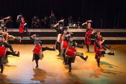 A drumming troupe dancing on a stage. The drums and parts of their costumes are a bright red.