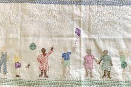 A piece of stitched fabric portraying families in diverse cultural clothing engaged in happy activities.