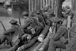 A group of armed soldiers watch a tank drive past.