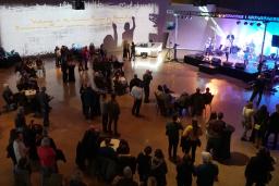 A crowd of people watches a band play on a brightly lit stage.