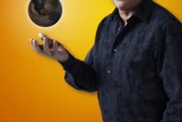 A man looking at the camera tosses up a globe.