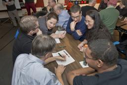 A group of excited people gathered around a table where one man is writing on a piece of paper.