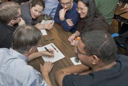 A group of excited people gathered around a table where one man is writing on a piece of paper.