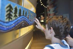 A child touches a painted panel with trees and tipis.