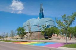 A rainbow crosswalk in front of the Canadian Museum for Human Rights on a sunny day