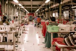 Garment workers sit at desks with sewing machines in a warehouse.