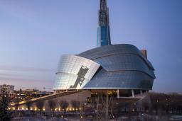 The exterior of the Canadian Museum for Human Rights, seen in the sunset against the city skyline.
