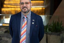 Walter Cassidy stands in front of the glowing alabaster ramps at the Canadian Museum for Human Rights. On his suit lapel, a small pin reads "Queer."