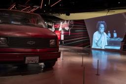 Red Chevrolet van in an exhibition space with video by Rage Against the Machine playing in the background.