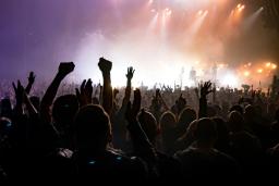 Concert-goers raise their hands in collective jubilation as a band plays on a brightly lit stage.