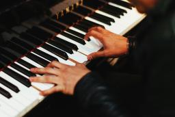 Two hands play the keys of a gleaming black Yamaha piano. The pianist, barely shown, wears a long-sleeved black top.