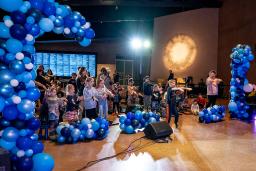 Kids dancing in a hall filled with blue balloons.