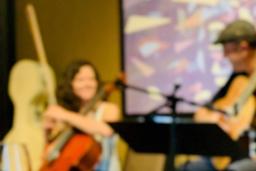 A cello player and guitar player chat and play music together in a café.