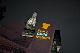 An image of an orange shirt with the text Every Child Matters is projected on an exterior wall of the Museum.