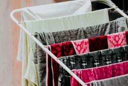 Garments are hung over a rack to air dry. The fabrics are grey, black, white and shocking pink.