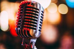 A performance microphone in the foreground reflects red and gold lights. Blurred in the background are patio lights.