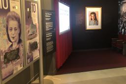A museum exhibit that resembles an old-fashioned movie theatre. On one side are large representations of a $10 Canadian banknote featuring a woman’s face.