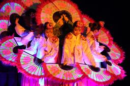 Korean dancers holding large, flower-patterned fans are grouped together so their fans form a circle.