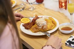 A person is sitting at a restaurant table eating waffles and bacon.