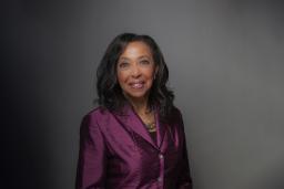 A portrait of a Black woman with long hair wearing a plum-coloured jacket.