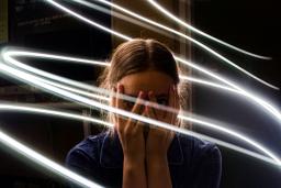 A teen girl holds her hands over her face and looks out stricken through her fingers. Bright while lines swirl around her.
