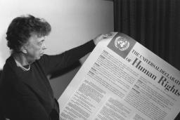 A person holds a large piece of paper covered with text and a large title reading "The Universal Declaration of Human Rights."