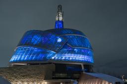 The exterior of the Canadian Museum for Human Rights is pictured at night. The building is lit up from the inside with vibrant deep blue lights.